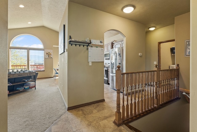 hallway featuring a textured ceiling, light colored carpet, arched walkways, vaulted ceiling, and an upstairs landing