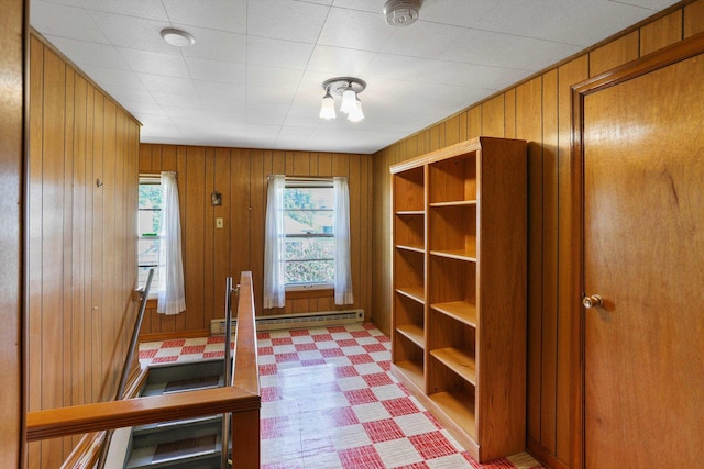 interior space featuring light floors, a baseboard heating unit, and wood walls