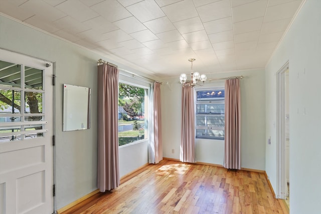 unfurnished dining area with crown molding, light wood-style flooring, and a notable chandelier
