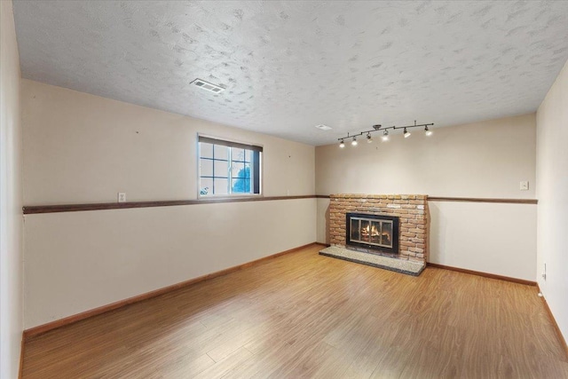unfurnished living room with a textured ceiling, visible vents, a fireplace, wood finished floors, and baseboards