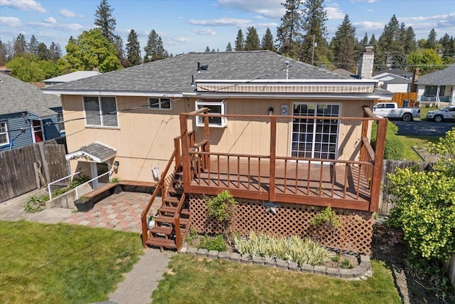 back of house with fence, a wooden deck, a shingled roof, a patio area, and a lawn