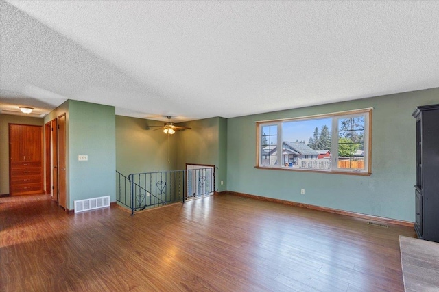 unfurnished living room with visible vents, baseboards, a textured ceiling, and wood finished floors