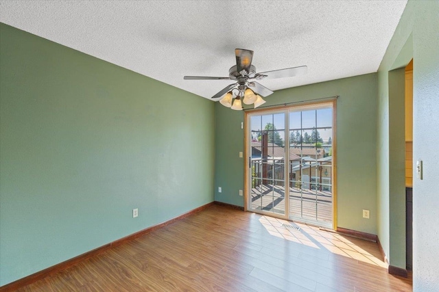 spare room with ceiling fan, a textured ceiling, visible vents, wood finished floors, and baseboards