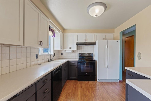 kitchen with decorative backsplash, light wood-type flooring, light countertops, under cabinet range hood, and black appliances