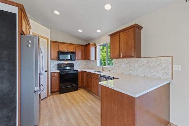 kitchen with vaulted ceiling, a sink, black appliances, a peninsula, and light wood-style floors