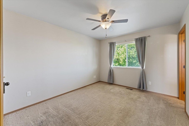 spare room featuring light colored carpet, baseboards, ceiling fan, and visible vents
