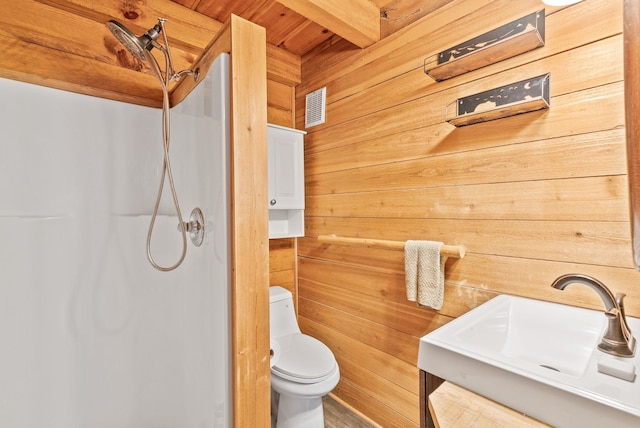 bathroom with wooden walls, toilet, walk in shower, and a sink