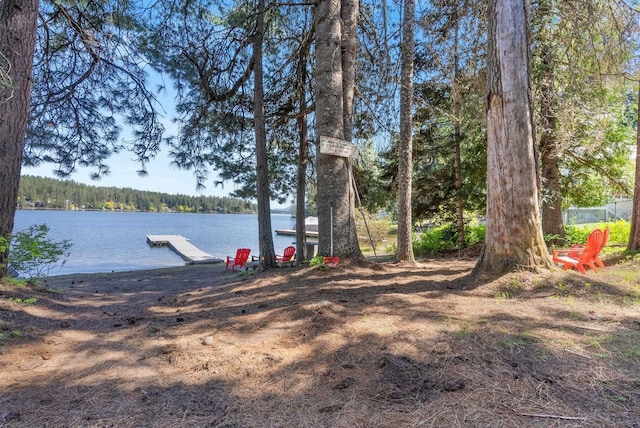 view of yard with a floating dock, a water view, and a wooded view