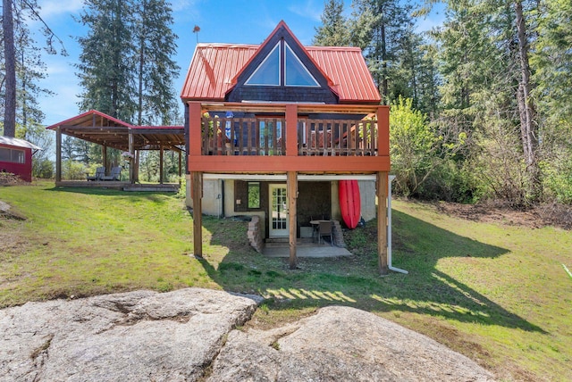 rear view of property featuring a lawn, a patio area, a wooden deck, and metal roof