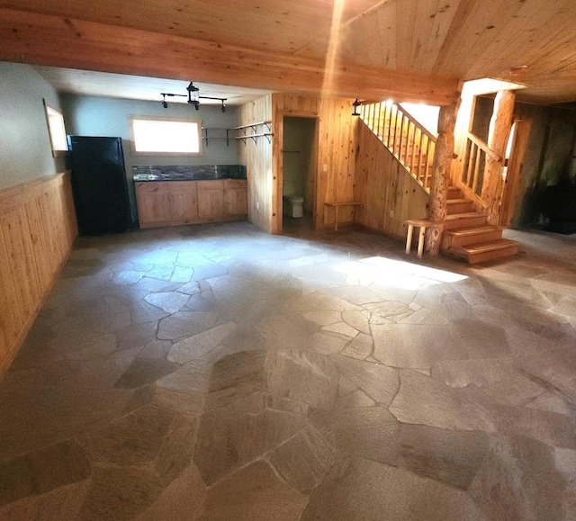 unfurnished living room with stone floors, wooden walls, stairway, a wainscoted wall, and wooden ceiling