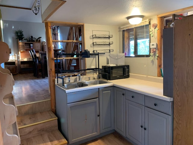 kitchen with black microwave, light wood-style floors, light countertops, gray cabinets, and a sink