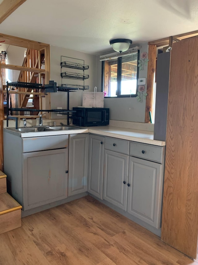 kitchen with black microwave, a sink, light wood-style floors, light countertops, and gray cabinetry