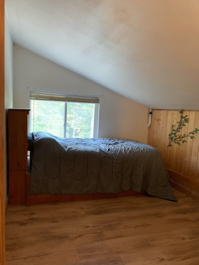 bedroom featuring wooden walls, wood finished floors, and vaulted ceiling
