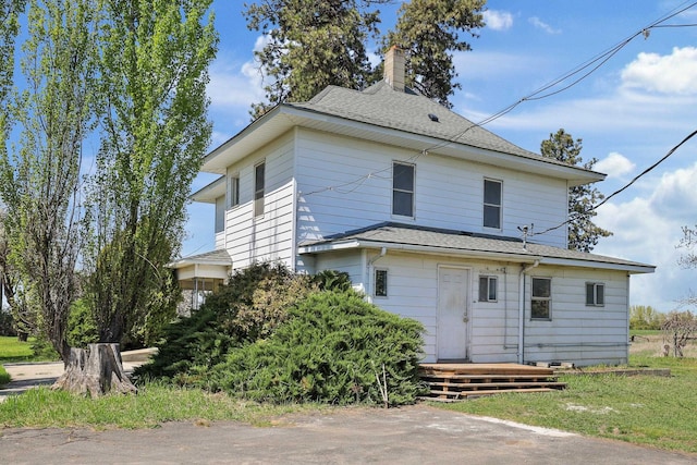 rear view of property with a shingled roof and a chimney