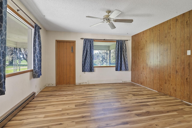 spare room featuring wood finished floors, ceiling fan, wooden walls, baseboard heating, and a textured ceiling