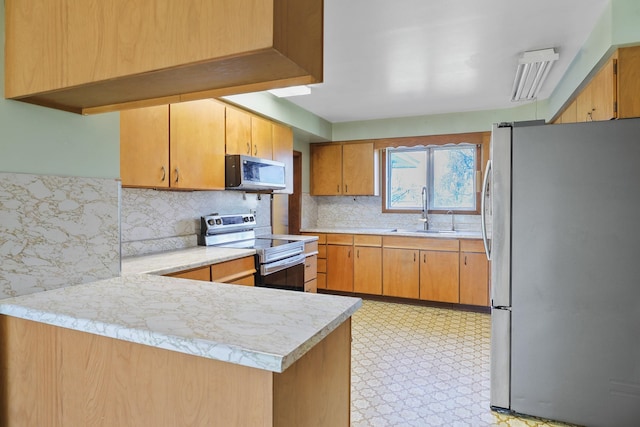 kitchen with a sink, light countertops, stainless steel appliances, a peninsula, and backsplash