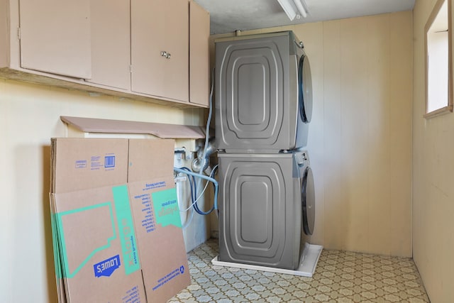 washroom with light floors, stacked washer and clothes dryer, and cabinet space