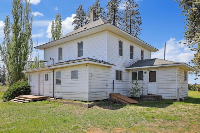 rear view of house featuring entry steps, a chimney, a lawn, and roof with shingles
