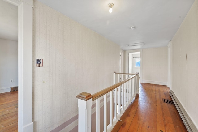 hallway featuring visible vents, a baseboard heating unit, hardwood / wood-style floors, and an upstairs landing