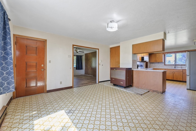 kitchen featuring freestanding refrigerator, a peninsula, baseboards, light countertops, and brown cabinets