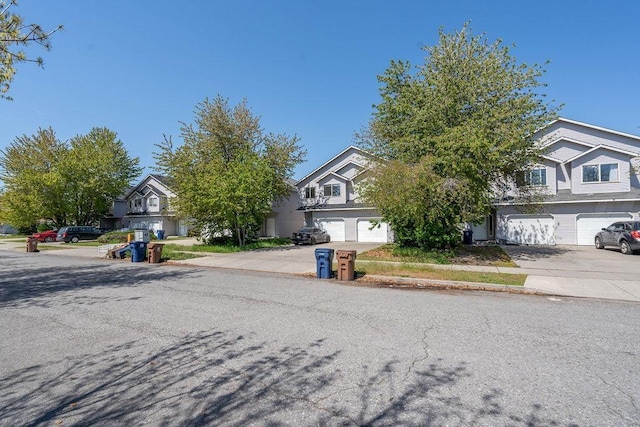 view of property hidden behind natural elements featuring driveway, a residential view, and a garage