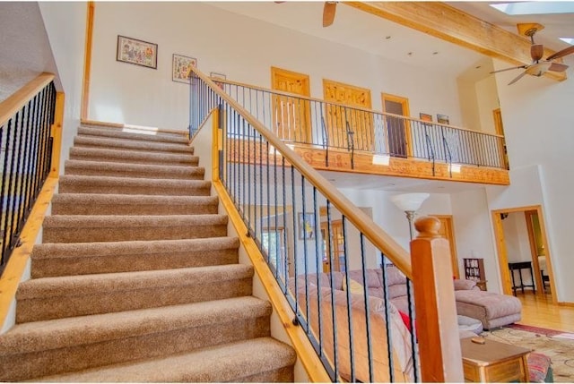 staircase featuring beamed ceiling, ceiling fan, a high ceiling, and wood finished floors