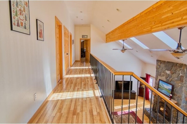 corridor with an upstairs landing, baseboards, vaulted ceiling with skylight, and wood finished floors