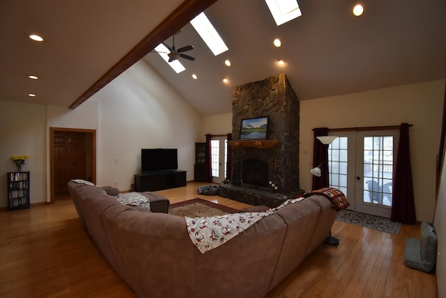 living room featuring wood finished floors, high vaulted ceiling, a skylight, a stone fireplace, and recessed lighting