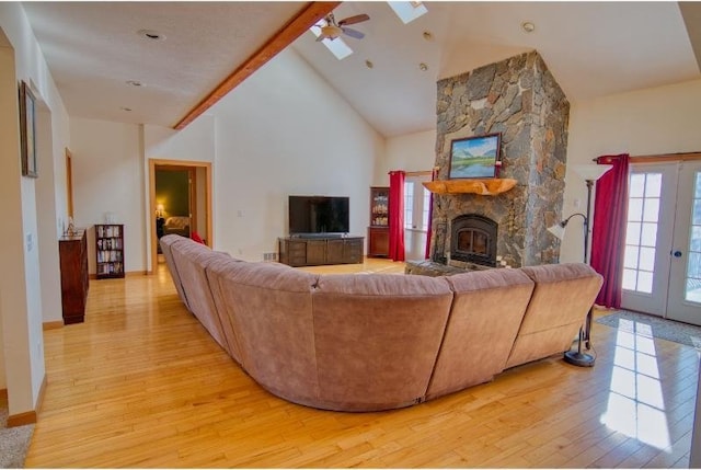 living area featuring a skylight, high vaulted ceiling, light wood-type flooring, a fireplace, and a ceiling fan