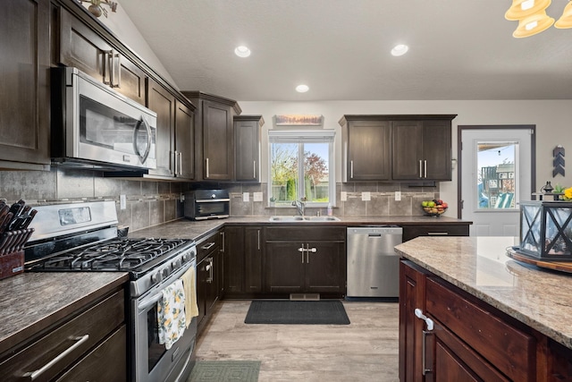 kitchen with light wood-style flooring, a sink, dark brown cabinetry, backsplash, and stainless steel appliances