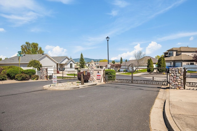 view of road with street lights, a gate, a residential view, a gated entry, and curbs