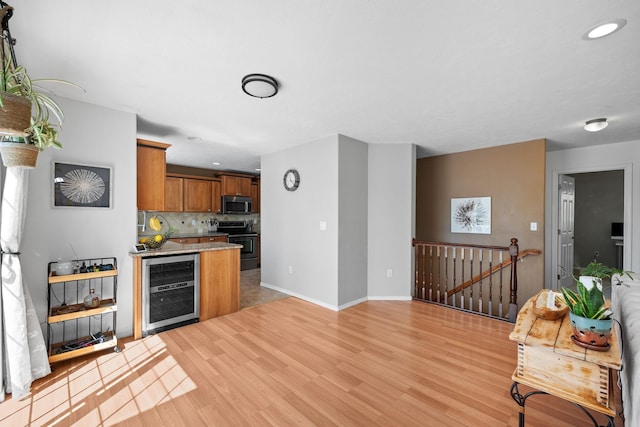 kitchen with beverage cooler, light wood-type flooring, stainless steel appliances, and brown cabinets