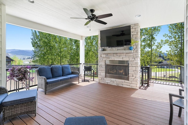 wooden deck featuring an outdoor living space with a fireplace, a ceiling fan, and a mountain view