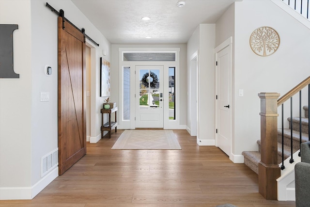 foyer entrance featuring baseboards, stairs, light wood-style floors, and a barn door