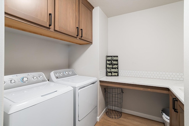 washroom featuring washing machine and clothes dryer, cabinet space, baseboards, and light wood-style floors