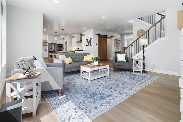 living room with a barn door, light wood-type flooring, recessed lighting, stairway, and baseboards