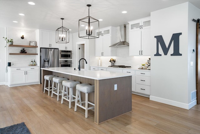 kitchen featuring recessed lighting, a kitchen island with sink, wall chimney range hood, stainless steel appliances, and tasteful backsplash