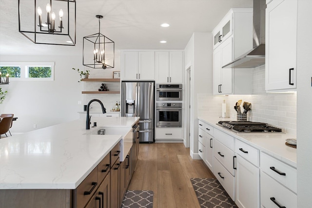 kitchen with a sink, stainless steel appliances, wood finished floors, recessed lighting, and wall chimney exhaust hood