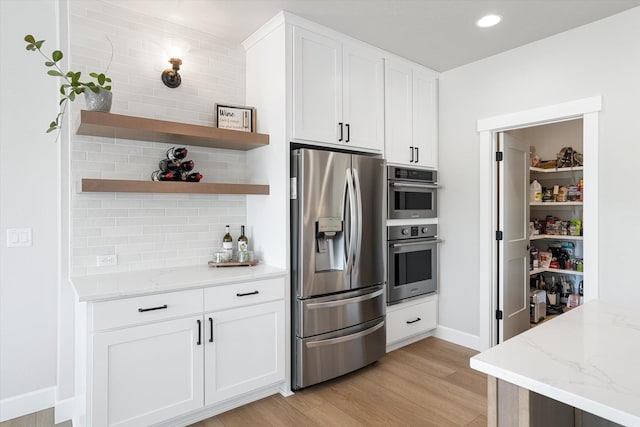 kitchen featuring light wood-style flooring, white cabinetry, decorative backsplash, light stone countertops, and appliances with stainless steel finishes