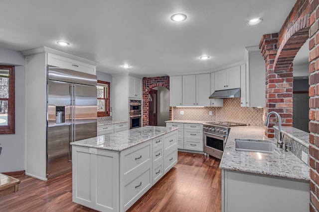 21724 N Perry Rd, Colbert, WA 99005 - kitchen with under cabinet range hood, a sink, high quality appliances, arched walkways, and tasteful backsplash