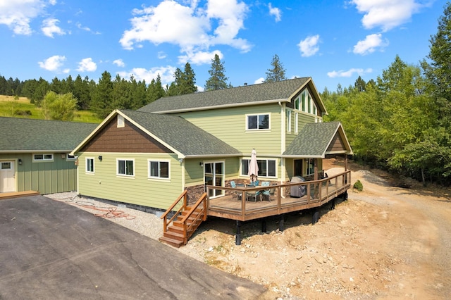 rear view of property with a shingled roof, driveway, and a wooden deck