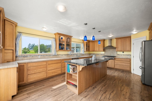 kitchen featuring a kitchen bar, appliances with stainless steel finishes, wall chimney exhaust hood, and wood finished floors