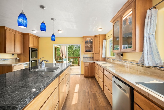 kitchen with light wood-style flooring, glass insert cabinets, hanging light fixtures, a sink, and appliances with stainless steel finishes