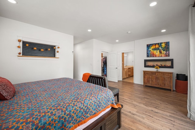 bedroom with ensuite bath, wood finished floors, a spacious closet, and recessed lighting