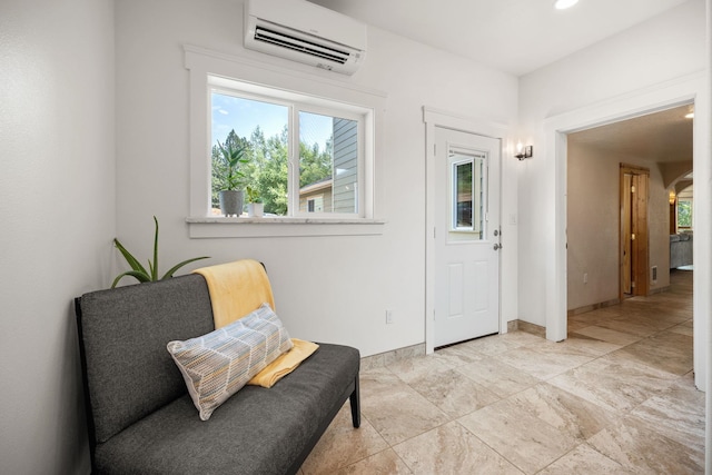 sitting room featuring a wall mounted AC, baseboards, and a healthy amount of sunlight