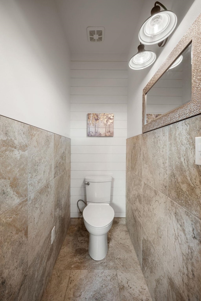 bathroom featuring toilet, tile walls, stone finish flooring, and visible vents