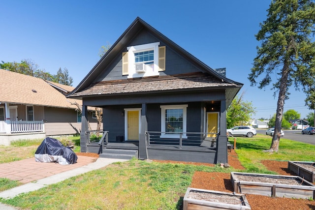 bungalow-style house featuring a front yard, covered porch, and a garden
