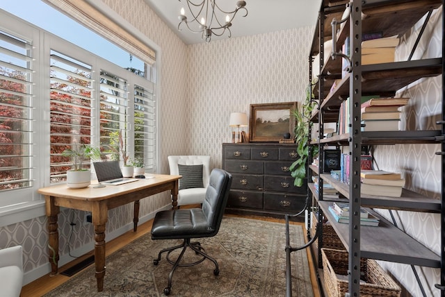 office area with an inviting chandelier, wood finished floors, wallpapered walls, visible vents, and baseboards