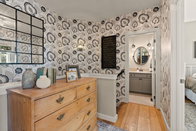 interior space featuring wallpapered walls, baseboards, wood finished floors, and vanity