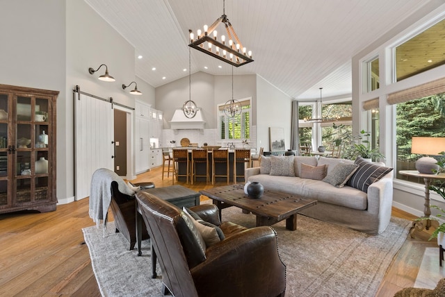 living room featuring a barn door, high vaulted ceiling, recessed lighting, light wood-style flooring, and a notable chandelier